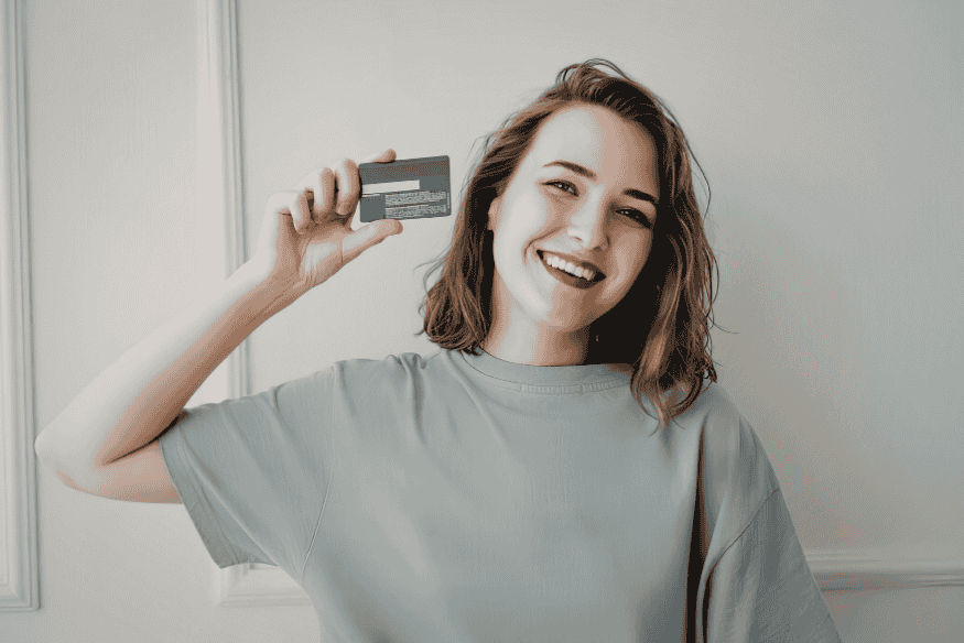 Smiling woman holding a credit card, symbolizing the credit-building benefits of being an authorized user on a well-managed credit card account.