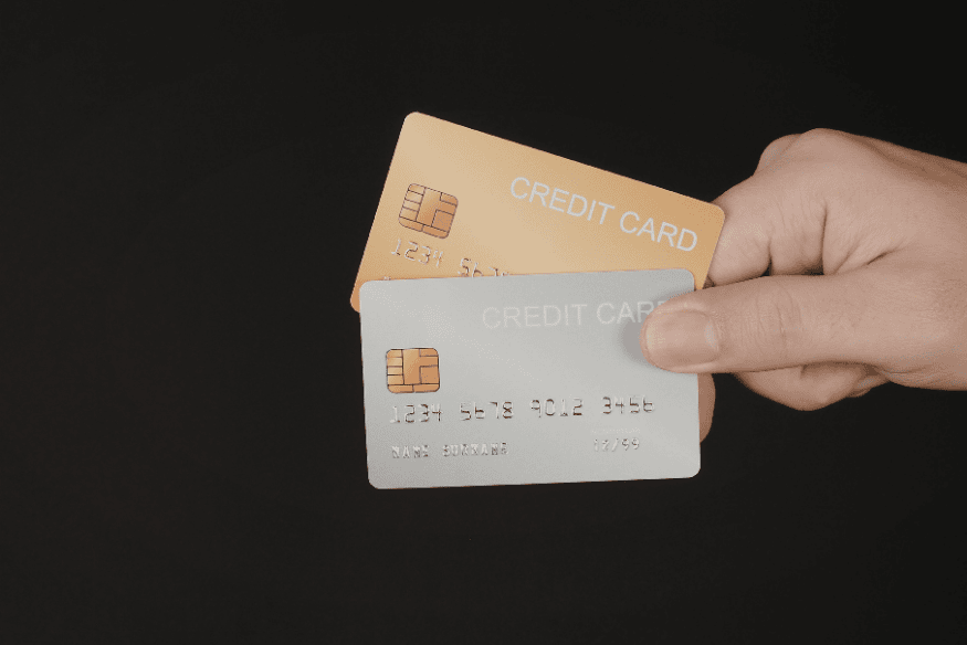 Hand holding two credit cards against a dark background, showing shared access and the risks of adding an authorized user to a credit card.