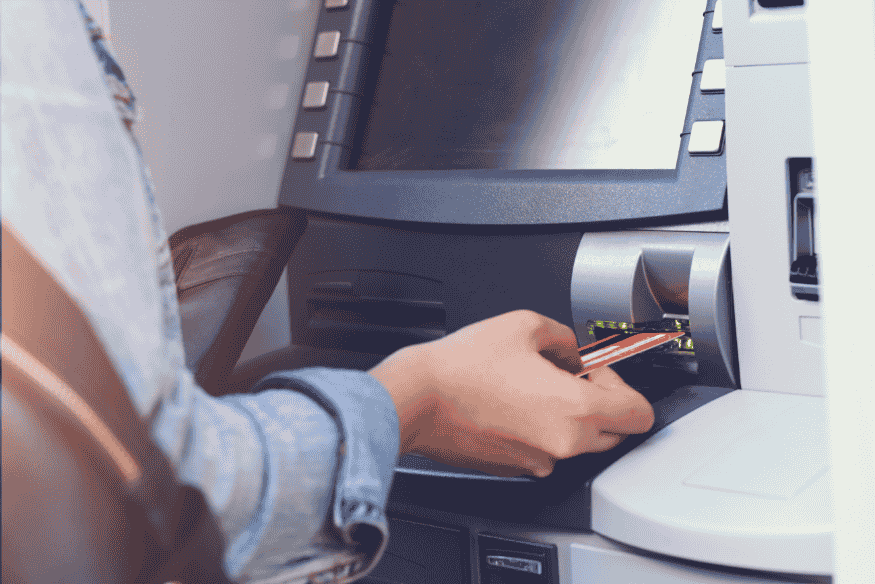 Withdrawing cash at an ATM using a debit card, showing how ATM fees can increase banking costs in the US