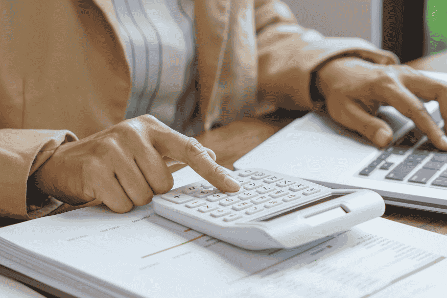 Person using a calculator and laptop to review financial documents, showing how to check a credit card statement for interest and extra charges.