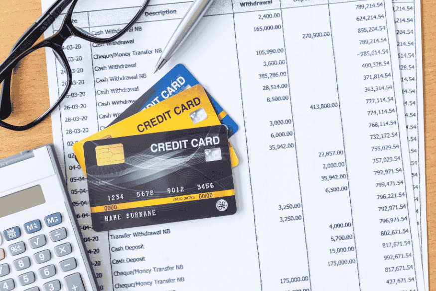 Credit cards placed on top of a financial statement with a calculator and glasses, representing credit card charges, balances, and hidden fees.