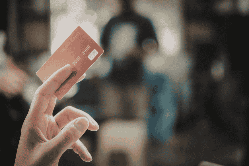 Hand holding a credit card in a shopping setting, representing credit card spending, balances, and utilization ratio.