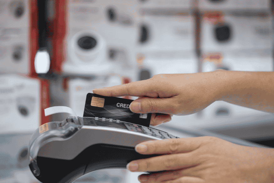 Person paying with a credit card on a card terminal, illustrating how credit card utilization works and affects available credit.