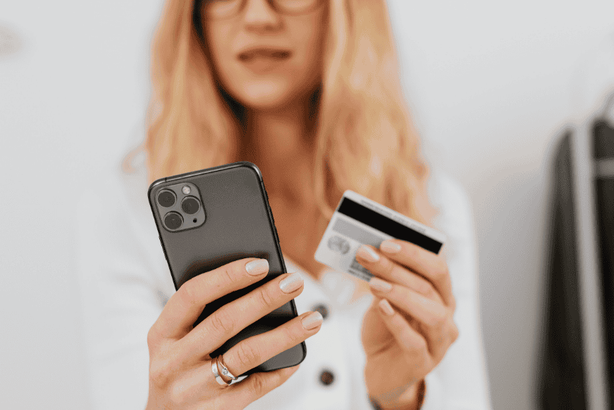 Woman holding a smartphone and credit card for an online purchase, showing digital spending and credit card utilization management.